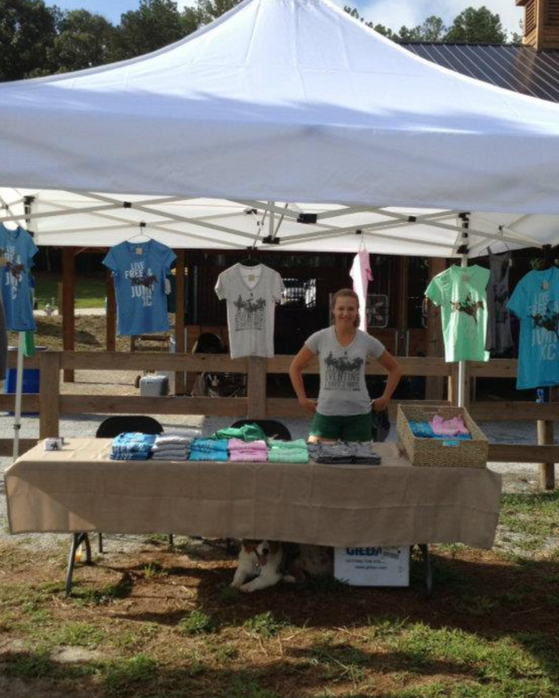 lead standing under a tent with shirts and a table